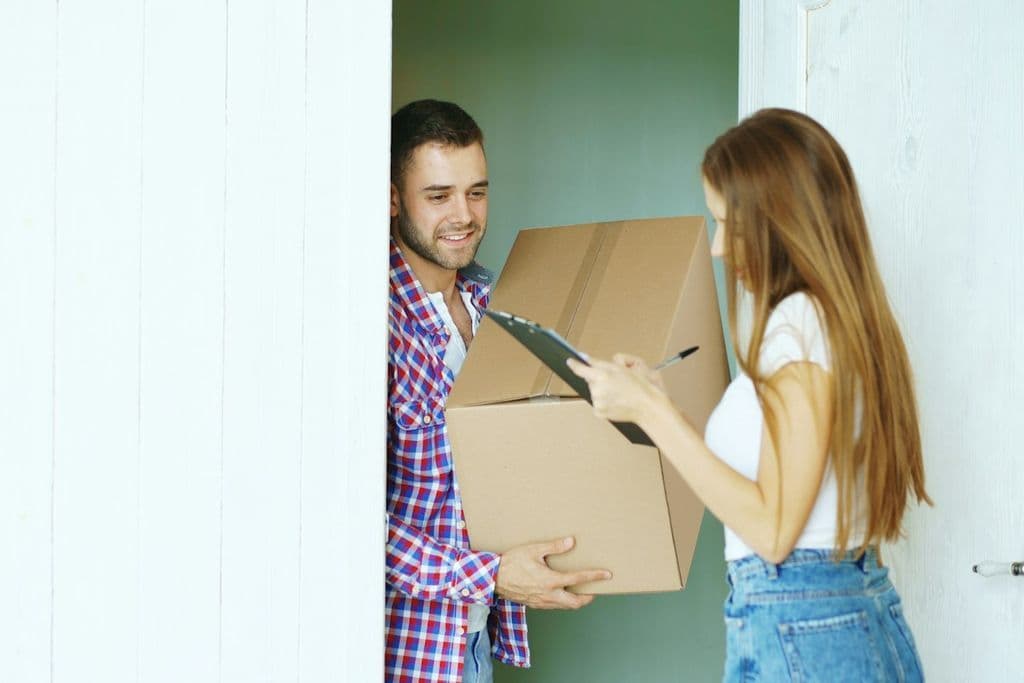 A man at a door handing a cardboard box to a woman who signs for the delivery