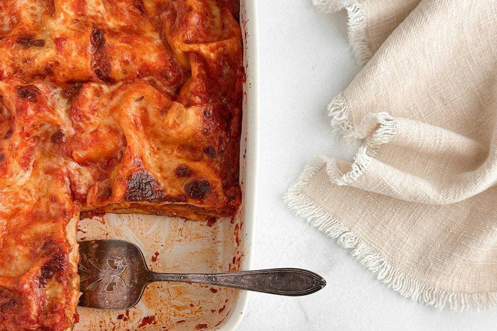 A home-baked lasagna in a white baking dish with a spatula, the kind of meal friends bring to new parents